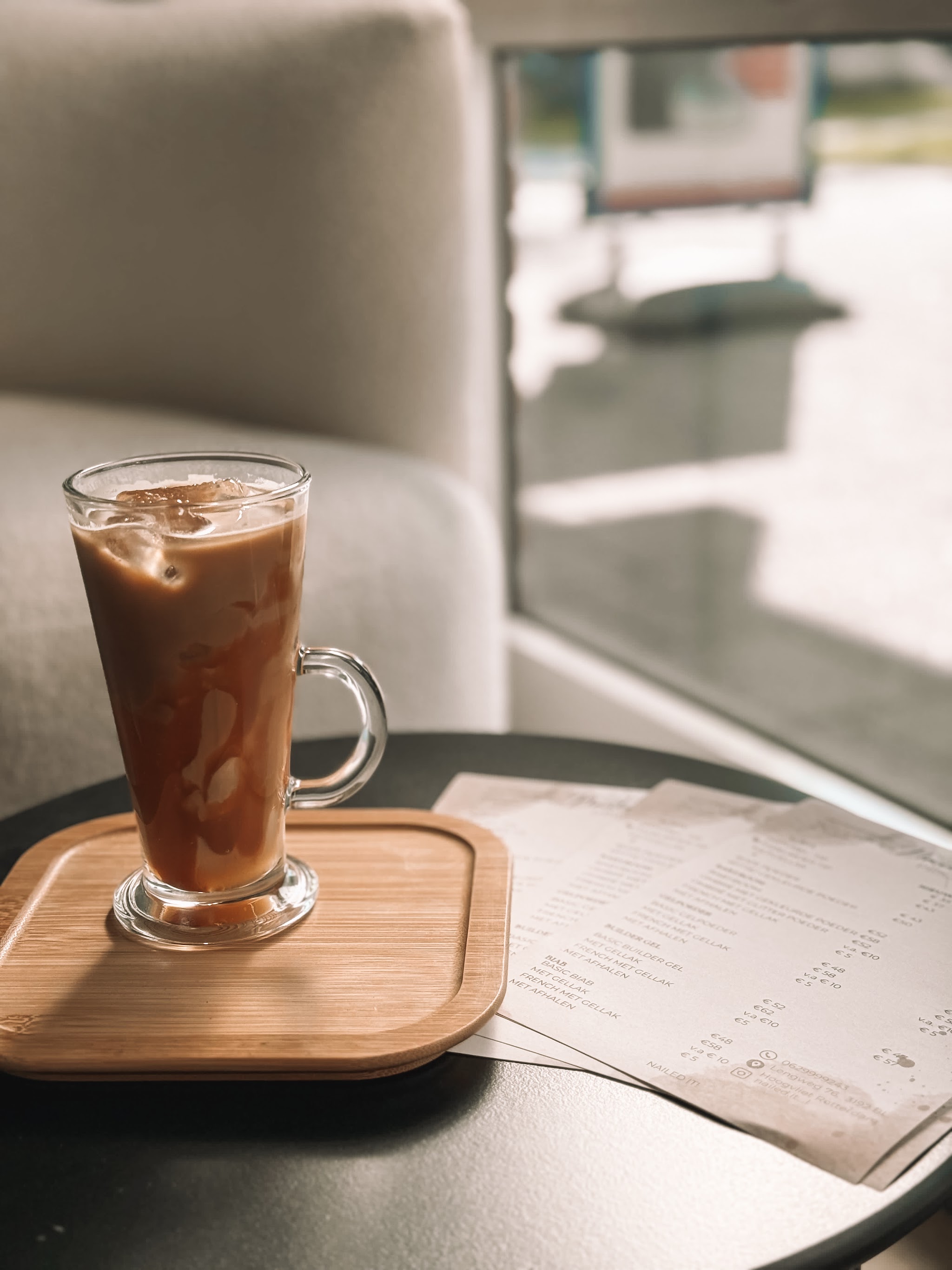 IJskoffie in een glas op een houten dienblaadje in de salon, met de bank op de achtergrond